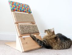 a cat laying on the floor next to a scratching board with its paws up against it