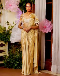 The flower patch on the shoulder seems like it is blooming from the joy of the season. The draped saree made with lightweight fabric materializes the concept of a fairy. The gold saree is embellished with beadwork and applique flowers all around to appear as if standing amongst flowers. Cold shoulder style blouse with back hook Pre-draped saree with a flower patch on the shoulder accentuated with beads and sequins embroidery. Metal zip on the saree. From Moledro’s Taabir collection. DELIVERY TIM Festive Gold Embellished Pre-draped Saree, Gold Pre-draped Saree With Resham Embroidery For Reception, Gold Pre-draped Saree With Sheer Dupatta For Navratri, Gold Pre-draped Saree With Gota Work For Wedding, Bollywood Style Pre-draped Saree In Raw Silk, Gold Pre-draped Saree For Reception And Festive Occasions, Gold Pre-draped Dola Silk Saree With Dupatta, Traditional Pre-draped Tissue Silk Saree With Dupatta, Traditional Drape Tissue Silk Pre-draped Saree For Reception