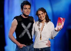 a man and woman standing next to each other in front of a blue background holding an award