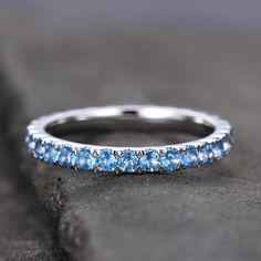 a white gold wedding band with blue topazte and diamonds on the side, sitting on a rock