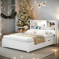 a white bed sitting in a bedroom next to a christmas tree with lights on it