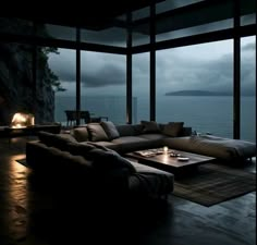 a living room filled with furniture and a fire place in front of a window overlooking the ocean