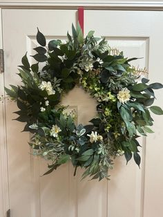 a wreath is hanging on the door with flowers and greenery around it's edges