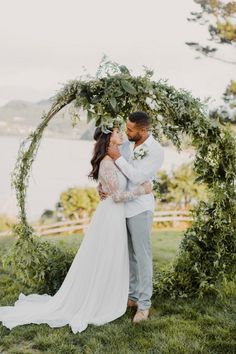 a bride and groom standing in front of an arch with greenery