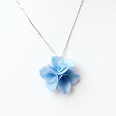 a blue flower is hanging from a chain on a white surface and it's attached to a necklace