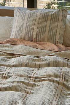 an unmade bed with striped sheets and pillows