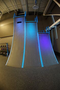 an indoor skateboard park with blue lights on the walls and ramps in front of it