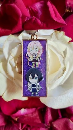 a necklace with anime characters on it sitting in front of pink flowers and white roses