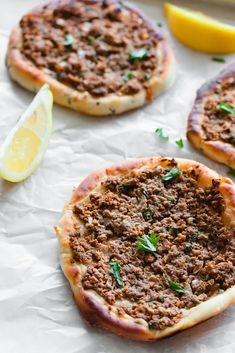 three small pizzas with meat and cheese on them next to a lemon wedged slice