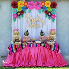 a table topped with cake and desserts next to a white wall covered in paper flowers