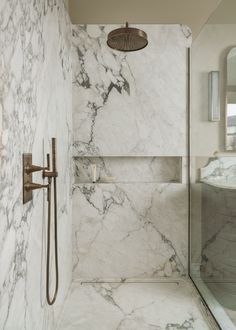 a bathroom with marble walls and flooring, shower head and hand held faucet