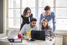 three people looking at a laptop screen while another person looks down on the table in front of them