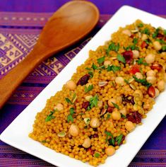 a white plate topped with lots of food next to a wooden spoon on top of a table