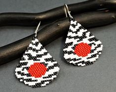 a pair of earrings with red and white designs on them sitting next to a branch