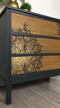 a black and gold dresser sitting on top of a hard wood floor next to a potted plant