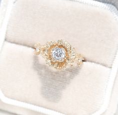 an engagement ring with a diamond center sits on a white velvet cushion in a box