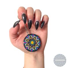 a woman's hand with black nail polish holding up a circular keychain