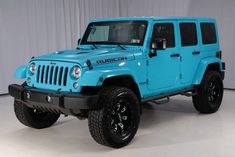 a bright blue jeep is parked in a room with white walls and black rims