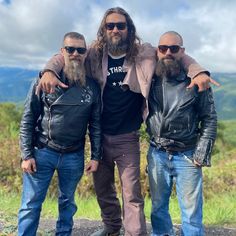 three men with long hair and beards standing next to each other in leather jackets