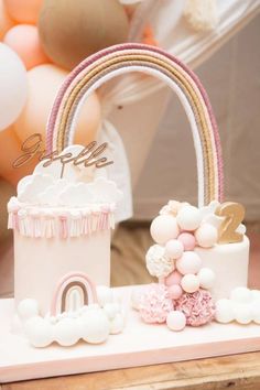 a pink and white cake sitting on top of a wooden table next to balloon decorations