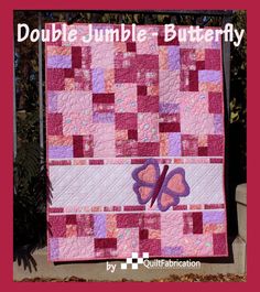 a pink and purple quilt with two butterflies on the front, sitting next to some leaves