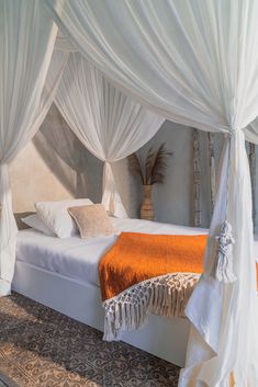 a bed with white drapes over it and an orange blanket on the bottom side