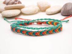 several different colored bracelets sitting on top of a white table next to some rocks