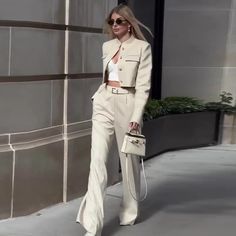 a woman is walking down the street wearing white pants and a blazer with matching heels