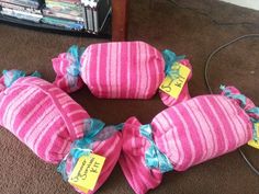 three pink and blue striped pillows with tags on them sitting on the floor in front of a book shelf