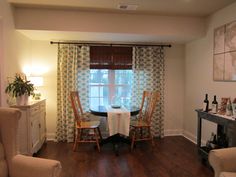 a dining room table and chairs in front of a window with the curtains pulled back