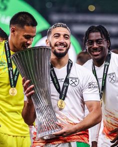 two soccer players are holding the trophy in front of their faces while another man looks on