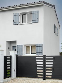 a white house with blue shutters on the front and side doors, along with a black fence