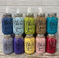 six painted mason jars with sayings in different colors and sizes, tied together to each other