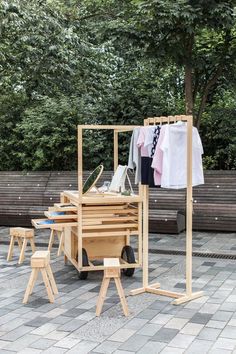 an outdoor clothing rack with clothes hanging on it's racks and four stools