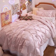 a bed with pink comforter and pillows in a white room filled with pictures on the wall