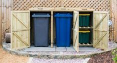 two blue trash cans are in the back of a wooden storage shed with doors open