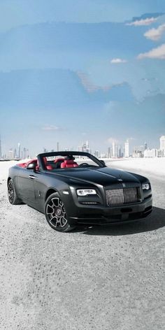 a black convertible car parked in the middle of an empty parking lot with buildings in the background