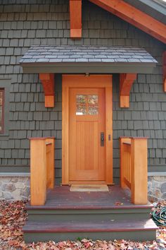 a wooden door on the side of a gray house with steps leading up to it