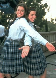 two young women dressed in plaid skirts posing for the camera with their arms stretched out