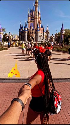 a man and woman holding hands in front of a castle at disney world with people walking around