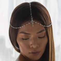 a woman wearing a silver head chain with crystal stones on the top and bottom, in front of a window