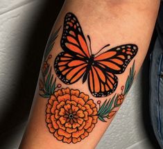 an orange flower and butterfly tattoo on the right arm, with leaves around it's edges