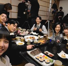 a group of people sitting at a table with food in front of them and cameras behind them