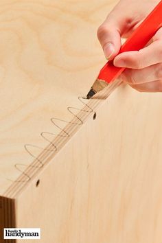 a person holding a pencil and writing on a piece of wood with the end of a ruler