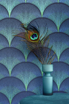 a vase with a peacock feather on it next to a wallpapered background in blue