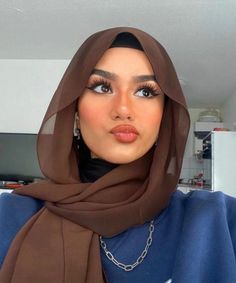 a woman wearing a blue shirt and brown shawl is looking at the camera with an intense look on her face