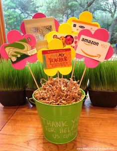 a green bucket filled with lots of food on top of a wooden table next to potted grass