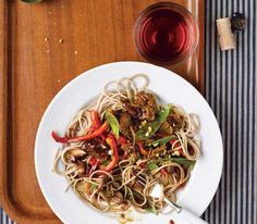 a white plate topped with noodles and veggies next to a cup of coffee