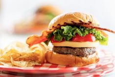 a hamburger with bacon, lettuce and tomato on a plate next to potato chips