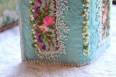 a close up of a decorative box on a table with flowers and lace around the edges